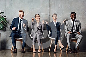 Happy multiethnic businesspeople sitting on chairs and cheering with clenched fists in