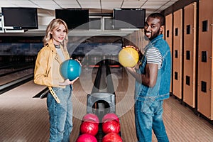 happy multiethnic couple with bowling balls looking at camera