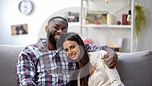 Happy multiethnic couple hugging and looking at camera, relaxing together