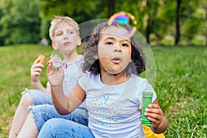 Happy multiethnic different age kids eating ice creams outdoor in summer. Cute positive hispanic girl enjoying blowing bulbs with