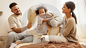 Happy multiethnic family mom, dad and child  laughing, playing, fights pillows and jumping in bed   at home