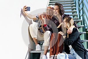 Happy multiethnic female best friends taking selfie sitting on stairs in