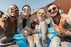 happy multiethnic friends in swimsuits and sunglasses posing