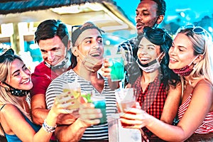 Happy multiethnic people drinking at night bar with open face masks - New normal summer concept with millenial friends having fun photo