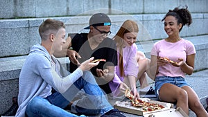Happy multiethnic teen friends eating pizza academy stairs, having fun together