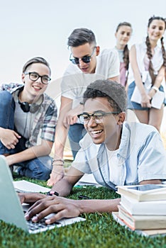 happy multiethnic teenage friends using laptop and studying