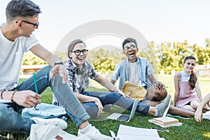 happy multiethnic teenagers sitting and laughing while studying together