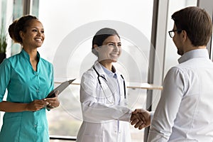 Happy multiethnic young doctor women shaking hands with medical boss