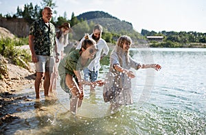 Happy multigeneration family on walk by lake on summer holiday, having fun in water.