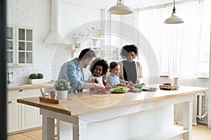 Happy multinational family with kids prepare vegetable salad in kitchen