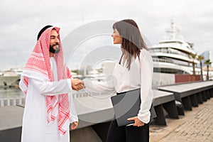 Happy multiracial business partners handshaking after successful signing contract at meeting in port