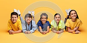 Happy multiracial children lying on floor and smiling, yellow background