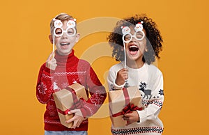 Happy multiracial children in warm knitted sweaters holding Christmas party glasses and gift boxes