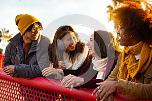 Happy multiracial college student friends laughing and talking enjoying sunny winter day. People having fun in city.