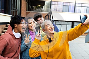 Happy multiracial college student friends take selfie with mobile phone laughing and having fun outside university.