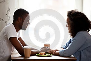 Happy multiracial couple holding hands, enjoying date in cafe