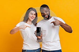 Happy multiracial couple holding and pointing at smartphone with black screen
