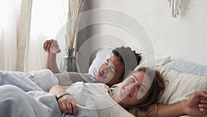 Happy multiracial couple lying in bed and laughing. Waking up together in the morning. Attractive young man and woman