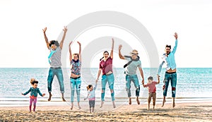 Happy multiracial families jumping together at beach holding hands - Summer vacation concept with young mixed race people having