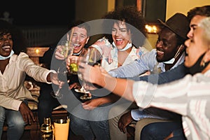 Happy multiracial firends cheering with cocktails at terrace party wearing face masks - Social distance during coronavirus