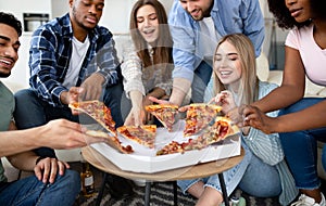 Happy multiracial friends chatting, eating pizza together, having small party at home