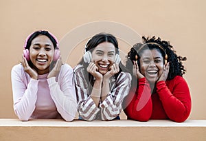 Happy multiracial friends having fun listening music with wireless headphones outdoor