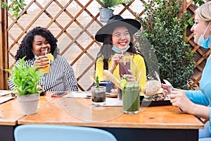 Happy multiracial friends having fun at restaurant outdoors with masks under chins - Focus on asian girl