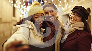 Happy multiracial friends taking selfie with mobile phone on winter holidays