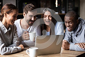 Happy multiracial friends watching funny comedy in cafe on laptop