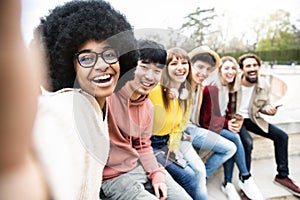 Happy multiracial group of friends taking selfie picture outside - International students having fun together sitting in college