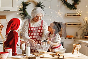 Happy multiracial kids help grandmother to cook Christmas cookies in kitchen during winter holidays