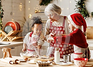 Happy multiracial kids help grandmother to cook Christmas cookies in kitchen during winter holidays