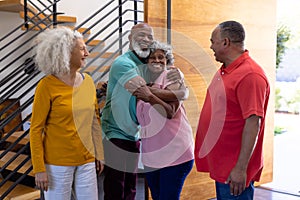Happy multiracial seniors welcoming friends while standing at doorway in retirement home