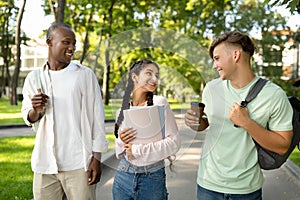 Happy multiracial university students walking together in park or in college campus, chatting outdoors during break