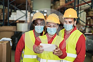 Happy multiracial workers taking a selfie inside warehouse while waring safety masks - Focus on woman face photo