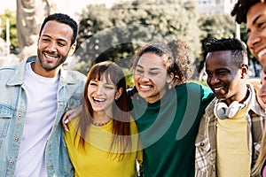 Happy multiracial young group of people hugging each other laughing at city
