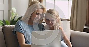 Happy mum and cute kid daughter having fun using laptop