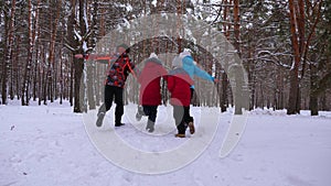 Happy mum and dad run with children through the winter forest. parents play with children in a snowy park in winter