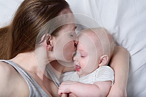Happy mum holding infant child on hands. Beautiful young mother kissing her baby