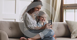 Happy mum and kid daughter laughing using looking at phone