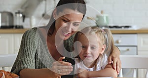 Happy mum and kid daughter laughing using smartphone at home