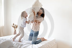 Happy mum and kid daughter play pillow fight on bed
