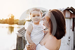 happy mum with little daughter outdoors on summer. Young mother with baby girl walk on beach near lake. Family holiday