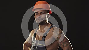 Happy muscular African male builder in hardhat smiling showing thumbs up