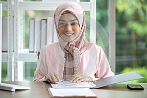 Happy Muslim business woman in traditional clothing smiling and working in office