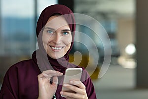 Happy muslim businesswoman in hijab at office workplace. Smiling Arabic woman working on laptop and talking on
