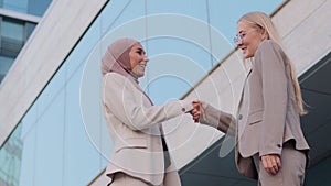 Happy muslim businesswoman sales manager in hijab shake hand of millennial caucasian lady client make deal with female