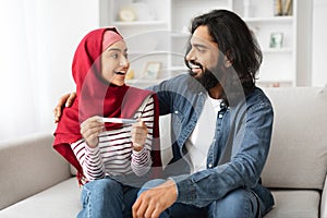 Happy Muslim Couple Holding Positive Pregnancy Test And Looking At Each Other