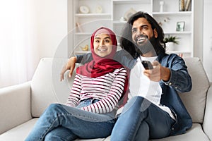 Happy Muslim Couple Watching Tv And Having Fun At Home Together