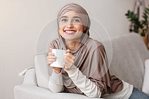 Happy muslim girl in hijab relaxing with tea at home